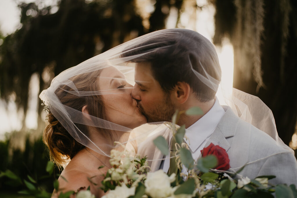 bride and groom kissing under veil at sunset