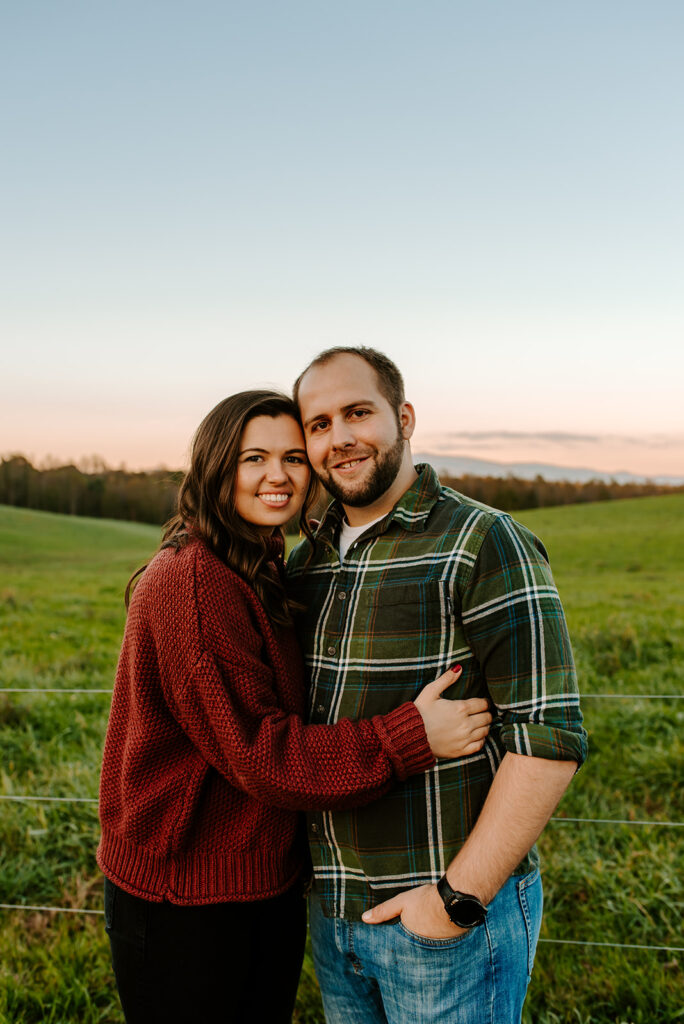 engaged couple smiling and holding each other in a field 