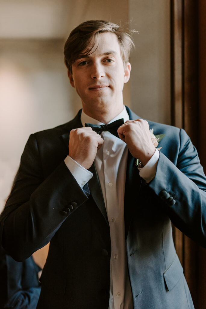 groom in navy suit straightening his bow tie