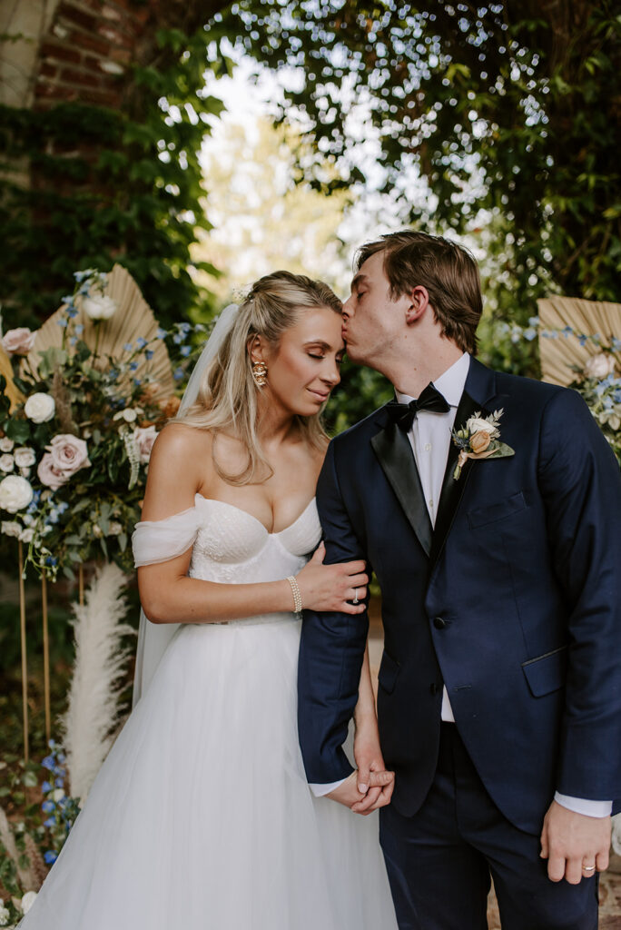 groom in blue suit kissing his bride on the forehead at summerour studio