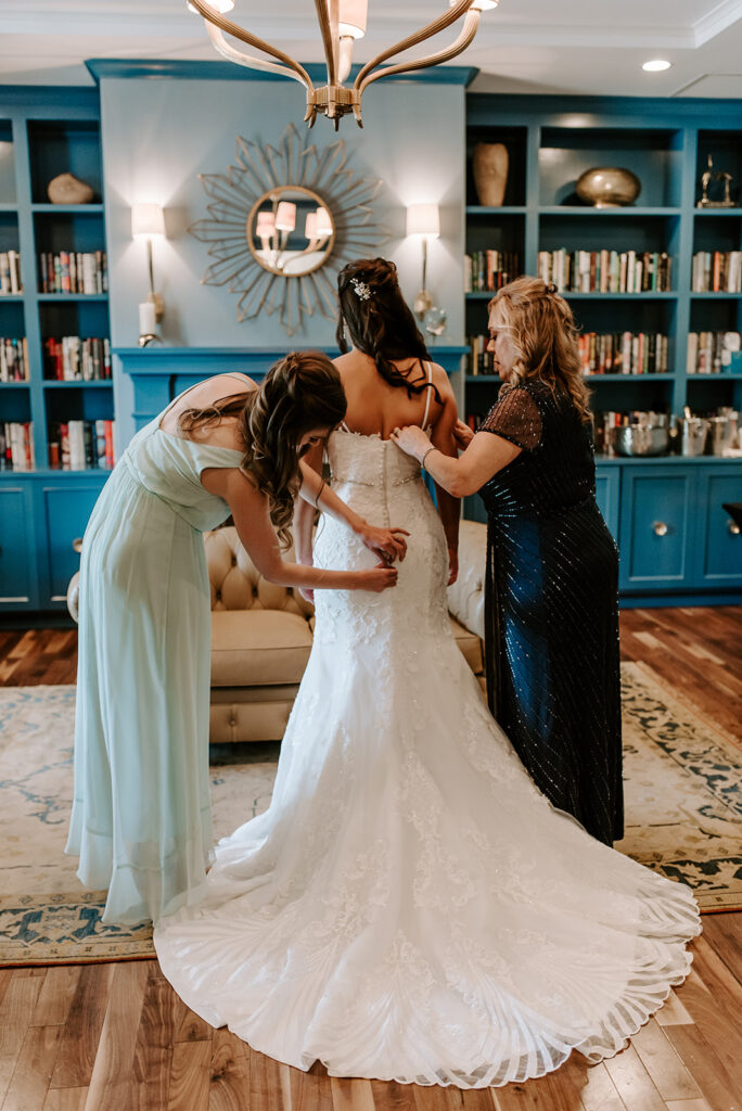mom and sister buttoning up the bride's wedding dress at the reserve club in aiken south carolina