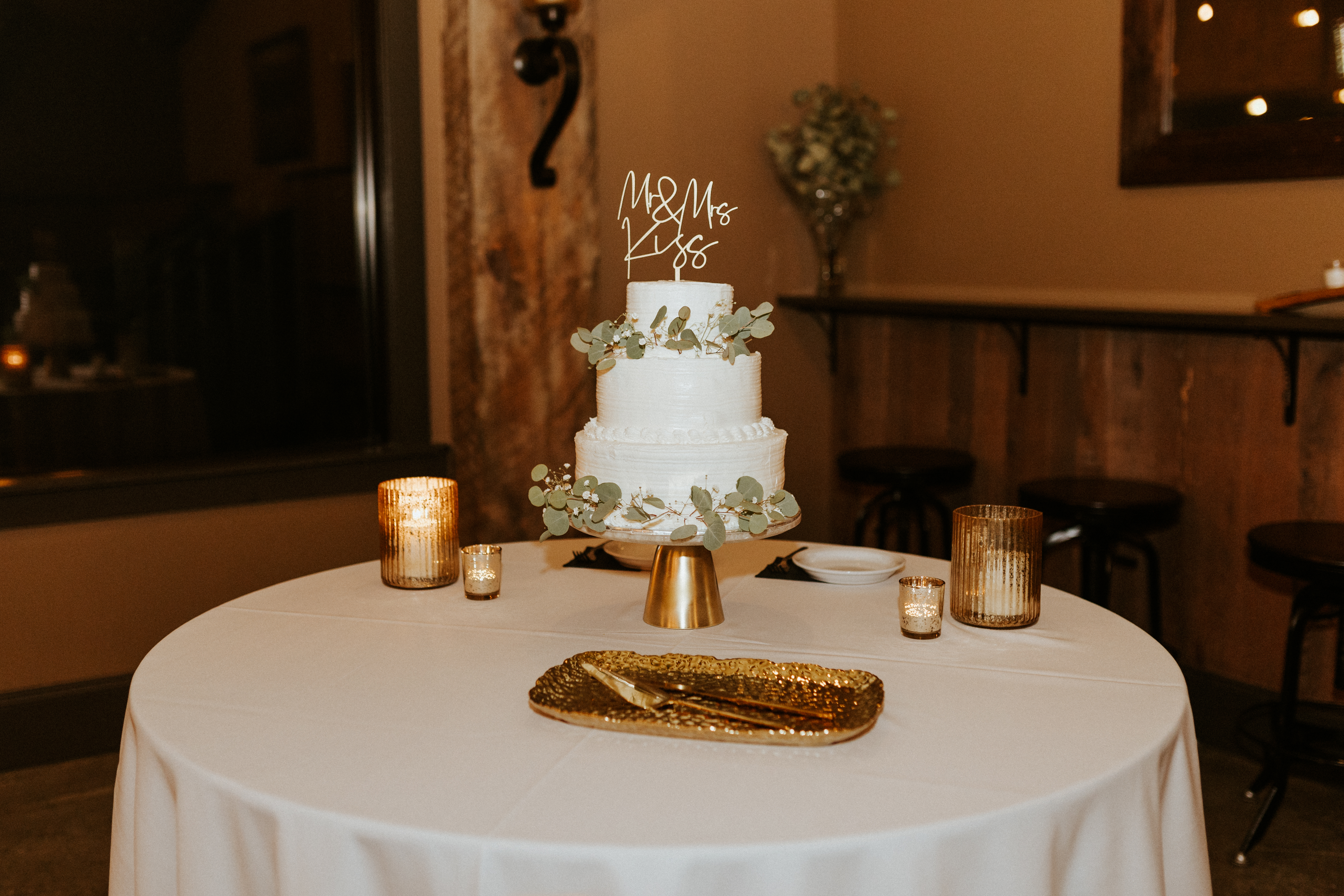 white wedding cake with simple greenery on gold cake stand at kaya vineyards
