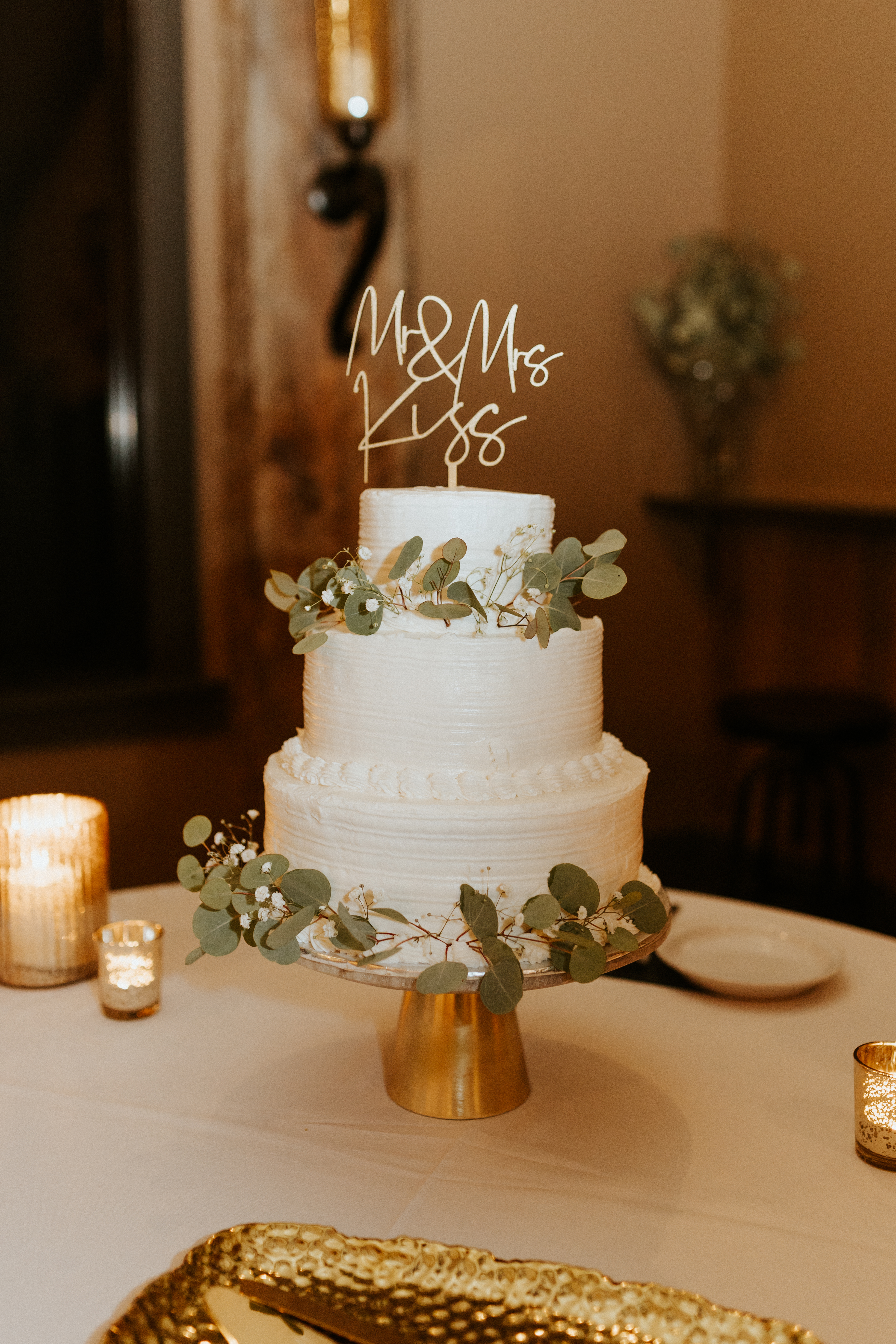 white wedding cake with simple greenery on gold cake stand
