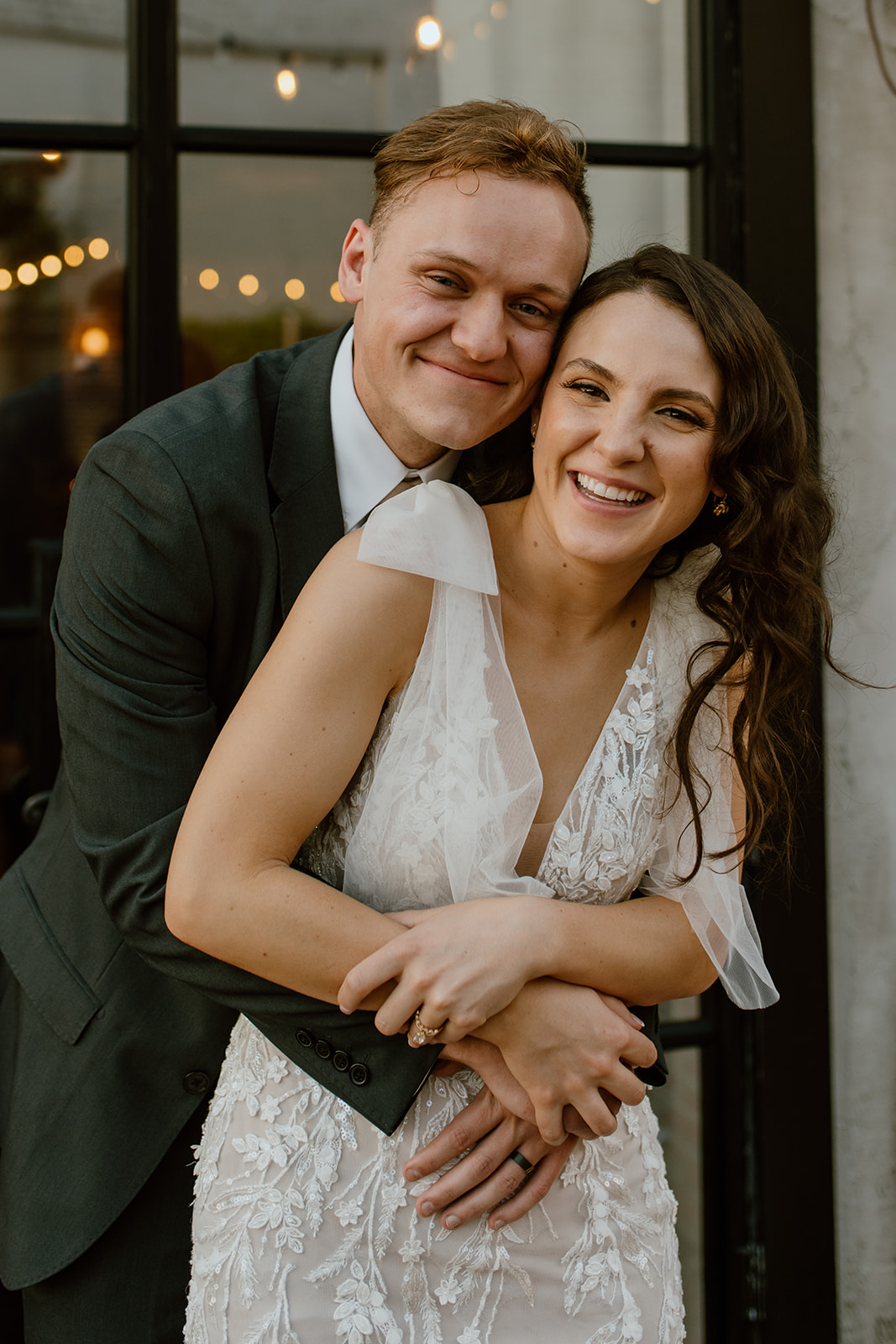 Groom hugging bride by window